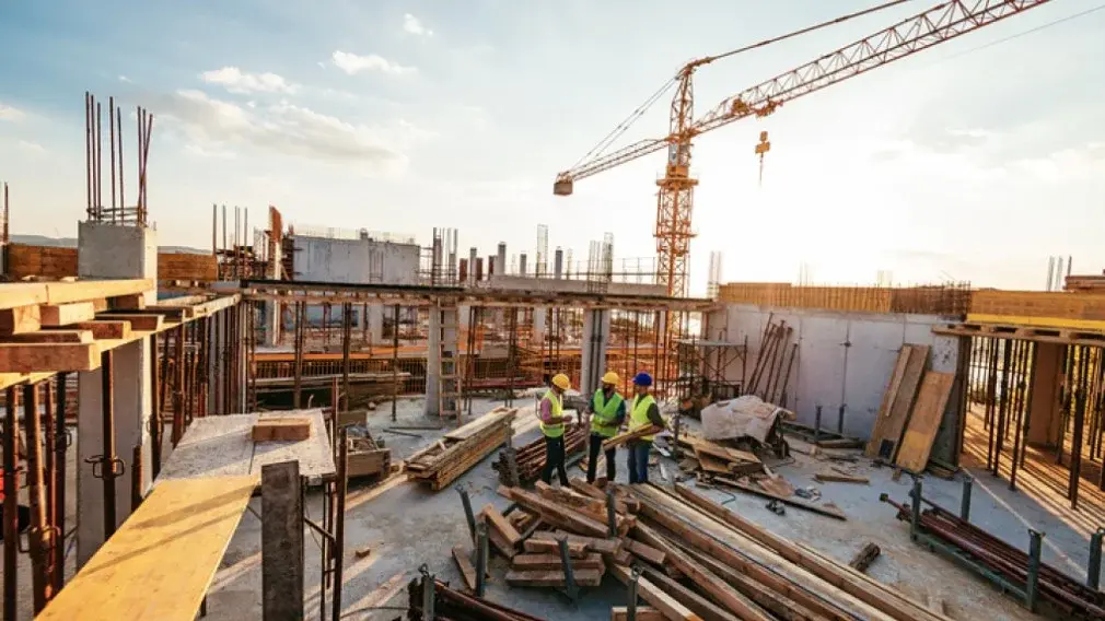 Construction workers reviewing site plans on an active build under a tower crane, golden hour